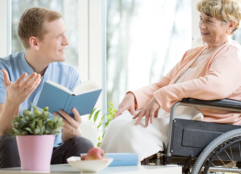 Male care assistant reading senior woman book